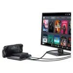 Een zwarte GPD WIN 5 handheld console wordt getoond in het dock en is via kabels verbonden met een monitor. De monitor toont de Steam OS-stijl interface met een raster van speltitels zoals Dead Cells, Deathloop, Portal 2 en Stardew Valley, wat de mogelijkheid van het apparaat illustreert om een desktop spelervaring aan te sturen.