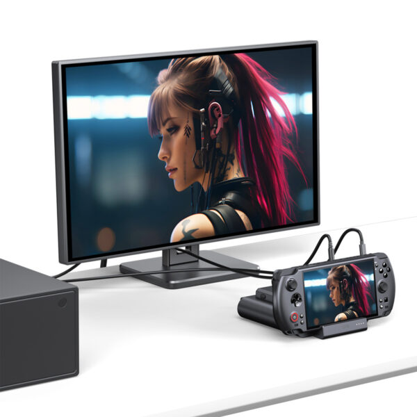 A desk setup showing the GPD WIN 5 docked and connected to an external monitor via cables. The same image of a female character with pink hair is displayed on both the small console screen and the large external monitor, demonstrating the dock's video output capability.