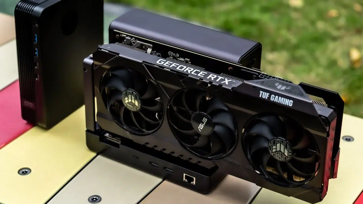 GeForce RTX graphics card with three cooling fans and 'TUF GAMING' branding installed in a compact PC case on a countertop outdoors.
