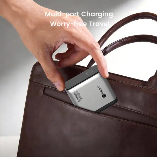 Tuvplānā redzama roka, kas ievieto sudraba daudzportu lādētāju brūnas ādas rokassomas sānu kabatā, fonā redzams teksts "Multi-port Charging, Worry-free Travel".